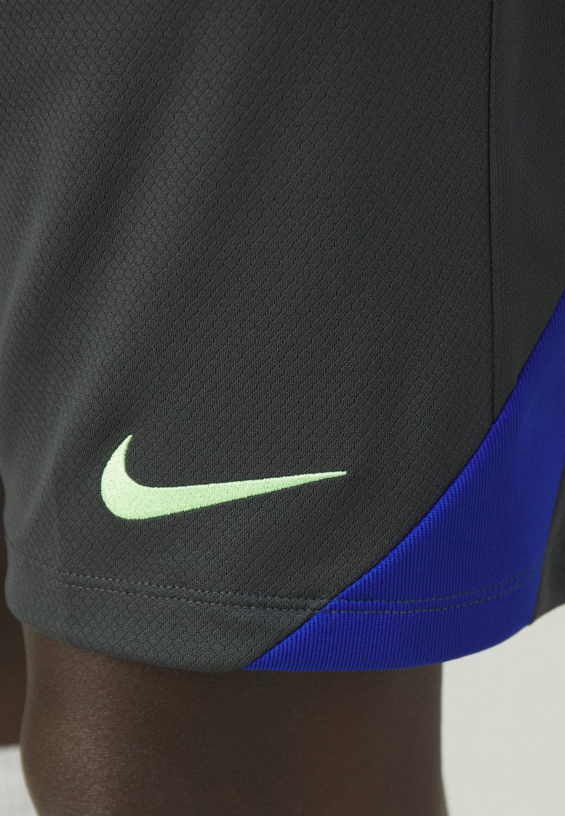 Pantalones cortos deportivos negros con una superficie texturizada. Presentan un logo de swoosh de Nike en verde y un acento azul royal a lo largo del costado.