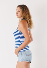 Canotta a righe blu e bianche con spalline sottili, abbinata a pantaloni corti in denim chiaro. La canotta presenta un design aderente e una texture liscia.