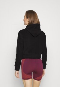 Felpa nera corta con cappuccio e orlo a coste, abbinata a pantaloni sportivi bordeaux con un motivo a strisce diagonali e logo.