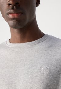 Sudadera gris de tela texturizada, con cuello redondo y un pequeño logo bordado en el pecho.