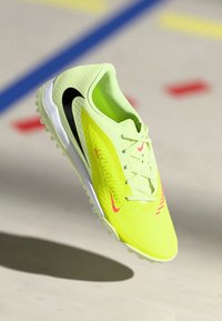 Jasnożółty but sportowy z czarnymi i różowymi akcentami, teksturowana cholewka, sznurowany design oraz formowana gumowa podeszwa z kolcami.