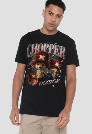 Junger Mann trägt ein schwarzes T-Shirt mit cartoonartigen Rentierfiguren mit roten Hüten und dem Text "Tony Tony Chopper Doctor."