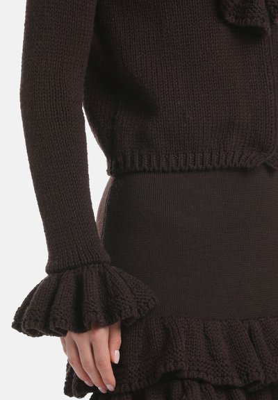 Temno rjav pleteni pulover z razširjenimi manšetami, ki vsebuje teksturirano šivovje, v kombinaciji z ujemajočo pleteno krilo z nabori.