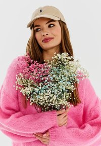 Różowy puszysty sweter, beżowa czapka i bukiet małych kwiatów w kolorze różowym, niebieskim i białym. Miękka tekstura, żywe kolory i naturalne detale.