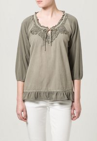 Blusa verde oliva con scollo rotondo, rifinitura in pizzo e coulisse. Presenta maniche a tre quarti e orlo ruffle nella parte inferiore.