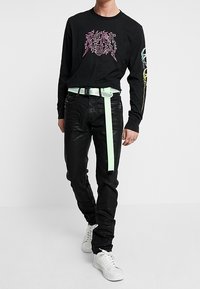 Svart långärmad skjorta med rosa grafisk design, åtsittande svarta jeans och vita sneakers. Har ett bälte i mintgrön färg.