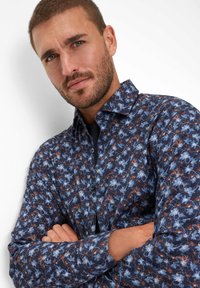Blauw shirt met bloemendessin, voorzien van een button-down kraag en lange mouwen. Heeft een marineblauwe achtergrond met ingewikkelde bloemenpatronen in blauw en bruin.