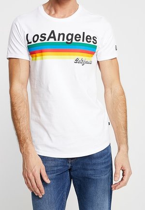 Biała koszulka z napisem "Los Angeles" nad poziomymi paskami w kolorach tęczy oraz "California" w stylu pisma odręcznego, noszona przez mężczyznę w niebieskich dżinsach.