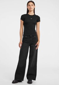 Maglietta nera aderente a maniche corte, abbinata a jeans neri a gamba larga. Tessuto liscio e design minimalista. Calzature: scarpe nere chunky.