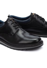 Zwarte leren schoenen hebben een gladde afwerking, een vetersluiting en een contrasterende rubberen zool met een grijze rand. De binnenkant heeft een blauwe voering.