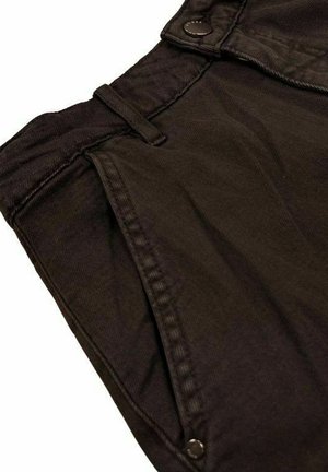 Primo piano di pantaloni marrone scuro che mostrano la vita, il passante per cintura, la tasca laterale e i dettagli con rivetti sulla trama del tessuto.