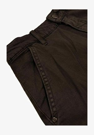 Primo piano di pantaloni marrone scuro che mostrano la vita, il passante per cintura, la tasca laterale e i dettagli con rivetti sulla trama del tessuto.