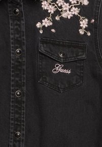 Czarna kamizelka z denimu z floralnym haftem w jasnoróżowym kolorze, z kieszenią na piersi i srebrnymi guzikami. Logo w stylu pisanego na kieszeni.