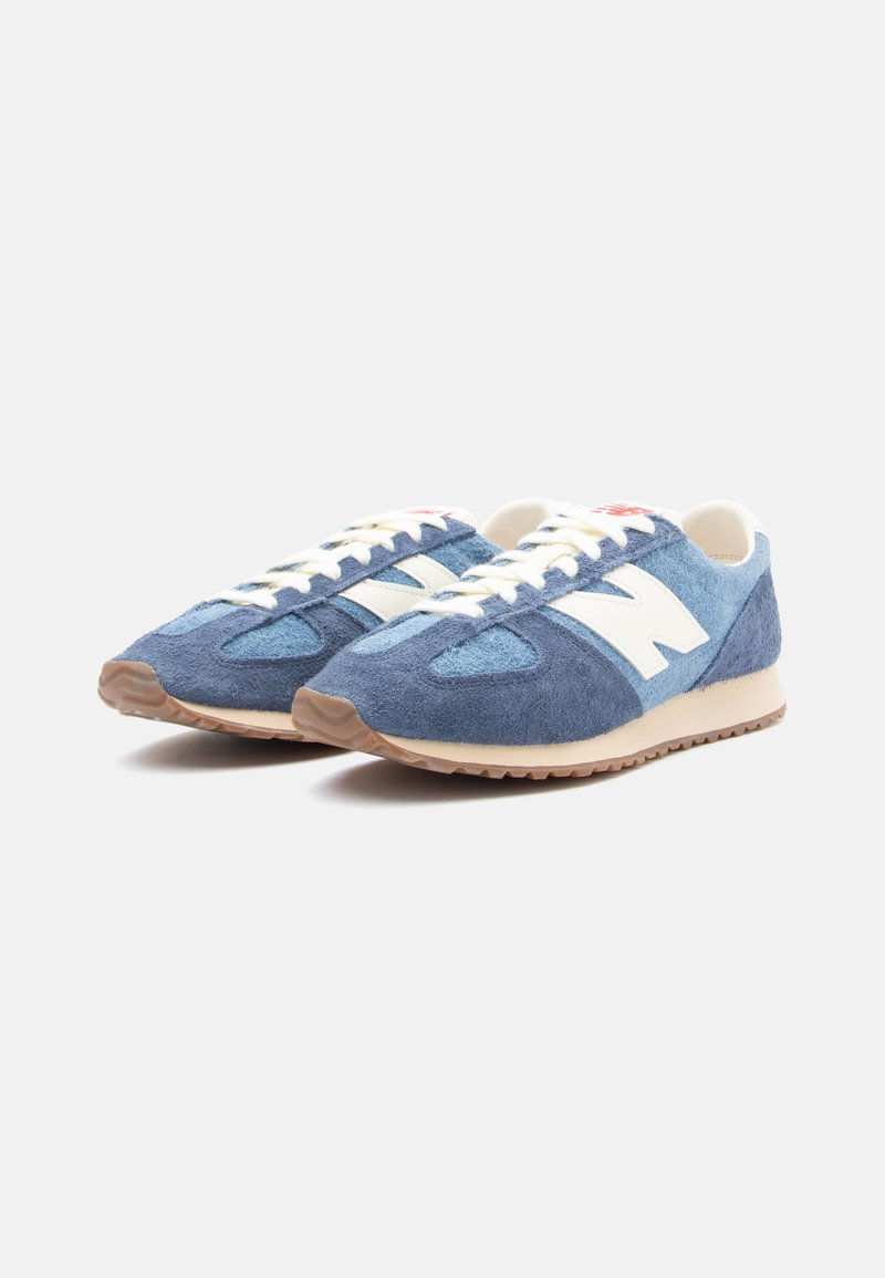 Blaue Wildledersneaker mit weißen Details, strukturiertem Obermaterial, runder Zehenkappe, Schnürdesign und Gummisohle. Besitzt ein kleines rotes Logo auf der Zunge.