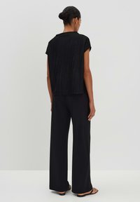 Haut noir avec un design texturé, manches courtes, associé à un pantalon noir ample. Les deux en tissu léger. Silhouette simple.