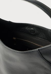 Μαύρη δερμάτινη τσάντα χειρός με υφή. Διαθέτει ευρύχωρο εσωτερικό, τσέπη με φερμουάρ και μαγνητικό κλείσιμο. Σχεδιασμός με λαβή από λεία επιφάνεια.