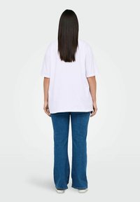 Camiseta blanca de gran tamaño con mangas cortas, combinada con jeans de campana azules. Tela suave, corte relajado y zapatos a la altura del tobillo.