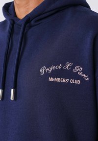 Marineblauwe hoodie met trekkoorden met metalen uiteinden en geborduurde tekst: "Project X Paris" en "MEMBERS' CLUB" in lichtroze.