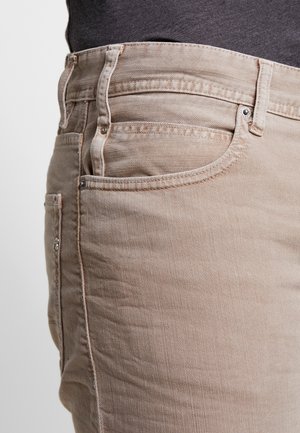Beżowe jeansy z denimu o teksturowanym wykończeniu, z klasycznym pięciokieszeniowym krojem, zapięciem na guziki i subtelnymi detalami szwów.
