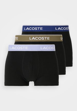 Three pairs of black boxer briefs featuring elastic waistbands in blue, olive green, and lavender with the "LACOSTE" logo in white.