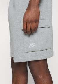 Gray cotton shorts with a side pocket, featuring a white Nike logo. Soft texture and relaxed fit, with stitched hems.