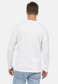 Hvid bomuld T-shirt med lange ærmer til mænd, med standard rund hals og grafiske designs på højre ærme. Synlige designdetaljer på ryggen.