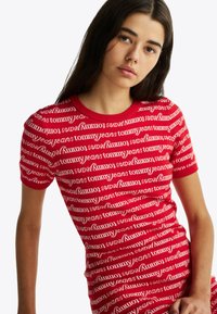 Rotes gestricktes T-Shirt mit einem sich wiederholenden weißen Textmuster "tommy jeans", im taillierten Design und mit Rundhalsausschnitt. Kurzärmelige Sichtbarkeit.