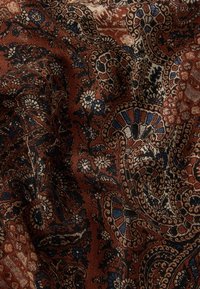 Barna mintás szövet, amely bonyolult paisley mintákat ábrázol krémszínben, kékkel és feketével. Texturált felület, gazdag, szövött megjelenéssel.