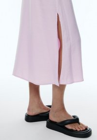Hellrosa Midikleid mit einem seitlichen Schlitz, kombiniert mit schwarzen Gummisandalen mit dickem Sohlen und einem geknoteten oberen Riemen.