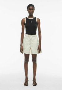 Zwarte mouwloze top met witte bies, lichtbeige shorts met een knoop aan de voorkant en zwarte sandalen met bandjes. Soepele stof, op maat gemaakte pasvorm.