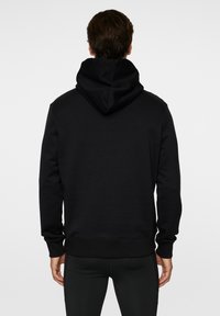 Musta huppari, jossa on kengurun tasku, joustavat hihansuut ja helma. Pehmeä kangas, jossa on suuri huppu ja rento istuvuus. Ei näkyviä logoja.