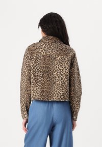 Cropped jas met luipaardprint in beige- en bruintinten, voorzien van een kraag, lange mouwen en knoopmanchetten. Draagt over een blauwe broek.