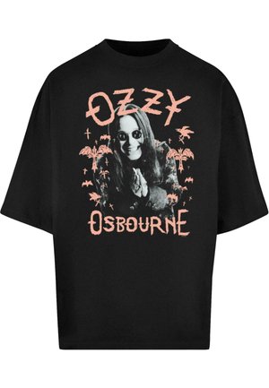 T-shirt nera oversize con stampa grafica di una figura con capelli lunghi e occhiali da sole, circondata da testo e illustrazioni rosa.