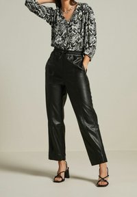 Schwarze Lederhose mit lockerer Passform und Seitentaschen, kombiniert mit einer Bluse in Schwarz-Weiß-Muster, die einen V-Ausschnitt und drei Viertelärmel hat.