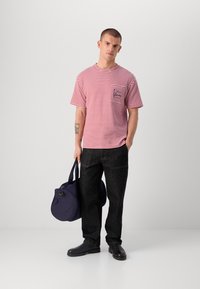 Rød og hvit stripete kortermet T-skjorte med brystlomme, kombinert med mørk denimbukser og en marineblå duffelbag. Svarte sko.