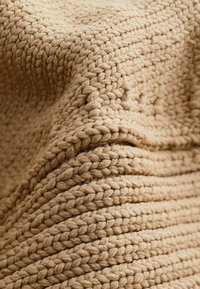 Karmiinbeige tekstuuriga kudum, pakse lõngaga, ribakujulise mustriga ja pehme, plushviimistlusega.