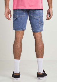 Denimshorts i ljusblått, med två bakfickor och en sidficka; matchat med vita strumpor och svarta skor.