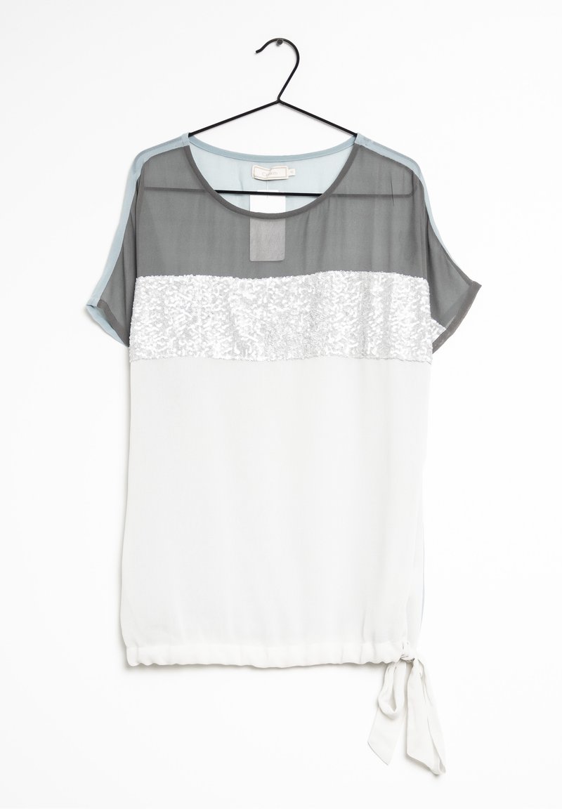 Blouse à manches courtes avec haut gris transparent, bande blanche texturée, bas blanc uni et lien latéral suspendu sur un cintre noir devant un fond blanc.