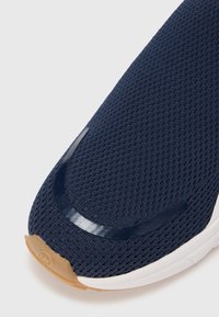 Tumesinise võrgustikuga spordijalats, mille varbakohal on sile ja läikiv tumesinine detail ning kummist pruuni tallaga. Mugavaks kandmiseks ümar ja kerge disain.