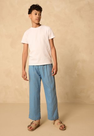 Witte katoenen T-shirt, lichtblauwe linnen broek en beige sandalen met bandjes. Eenvoudig ontwerp, ontspannen pasvorm en gladde textuur.