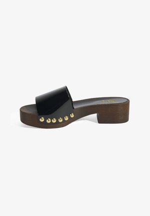 Sabot noir avec un talon en bois épais et une bride lisse et brillante. Présente des clous décoratifs dorés le long du bord extérieur.