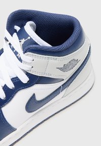 Baskets montantes Air Jordan blanches et bleu marine avec lacets visibles, col rembourré, logo Nike swoosh et logo aile Air Jordan sur le côté.