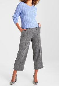 Lichtblauwe kabelgebreide trui gecombineerd met grijze, gestructureerde wijde broekspijpen en zilveren hoge hakken. Eenvoudig, modern ontwerp met strakke lijnen.