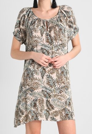 Vrouw draagt een korte mouw, knielange jurk met een beige achtergrond en een patroon van bruine, groene en blauwe palmbladeren.