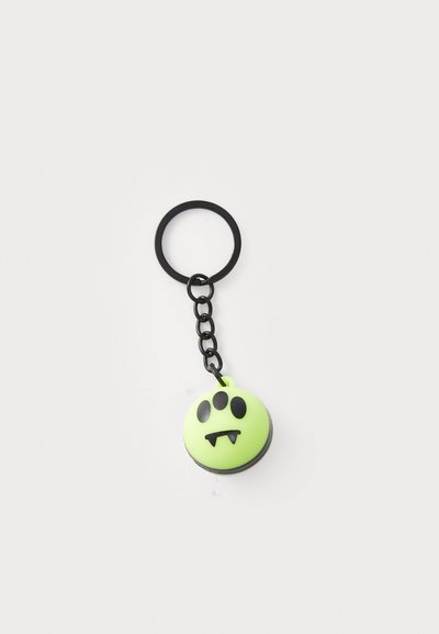 Portachiavi di gomma verde a forma rotonda, con un volto di mostro nero con tre occhi e zanne, attaccato a una catena di metallo nera e anello.
