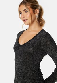 Zwarte, glanzende getailleerde lange mouwtop met een diepe V-hals en geribbelde textuur, die een slanke silhouet en soepele stof laat zien.