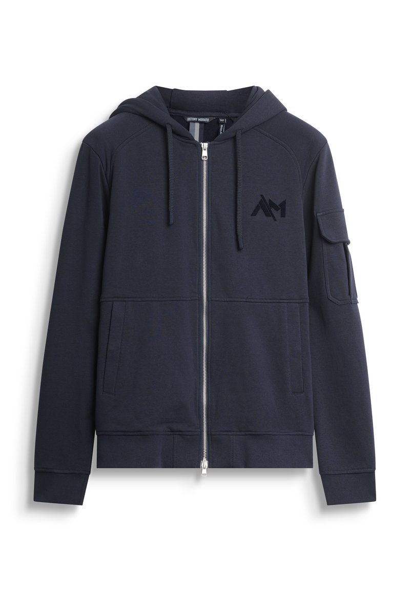Felpa con zip di colore blu navy realizzata in tessuto morbido, dotata di cappuccio, tasche frontali e una tasca sul braccio sinistro con dettaglio logo nero.
