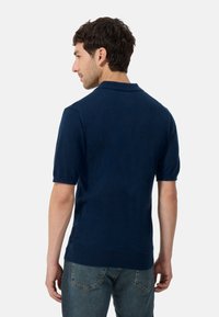 Marinblå kortärmad pikétröja med strukturerad tyg, ribbad krage och rak nederkant, i kombination med ljusblå denimjeans.