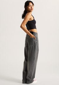 Top corto nero abbinato a jeans grigi a vita alta e dal taglio morbido. Presenta tasche frontali e un design rilassato. Tessuto texturizzato.