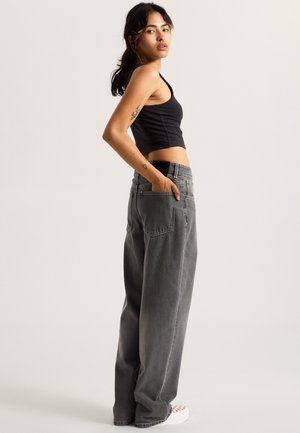 Svart kortärmad linne i kombination med högmidjade, löst sittande grå jeans. Har framfickor och en avslappnad design. Texturerad tyg.